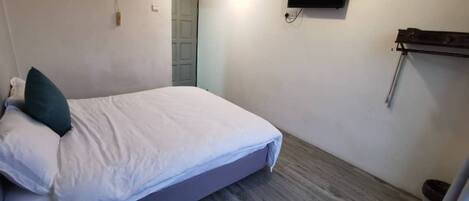 A bedroom with a bed, an air conditioning unit, a mounted TV, and a wooden floor.