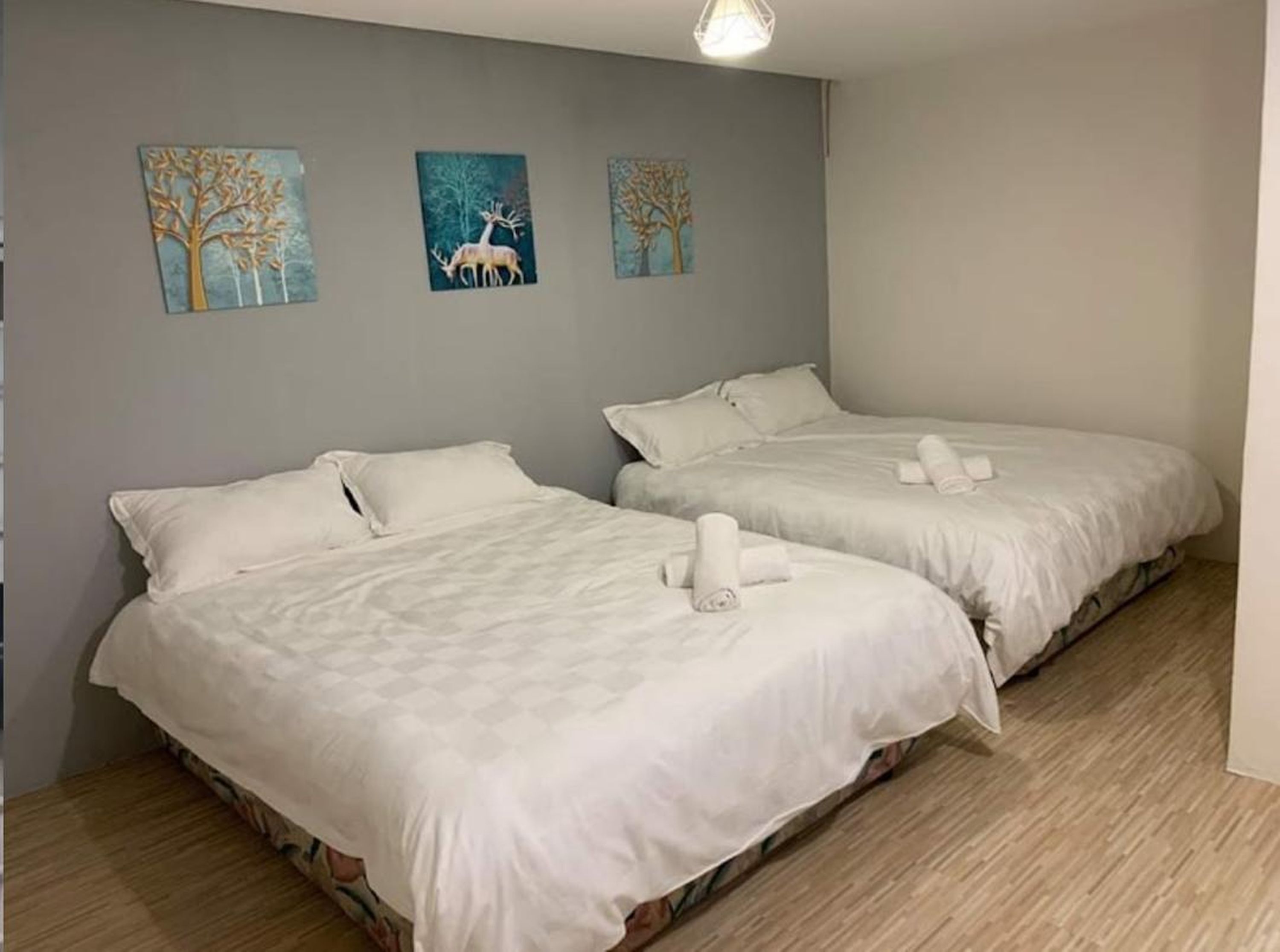Une chambre d’hôtel avec deux lits, chacun équipé de draps et de serviettes blancs. Trois tableaux sont accrochés au mur et représentent des arbres et des cerfs.