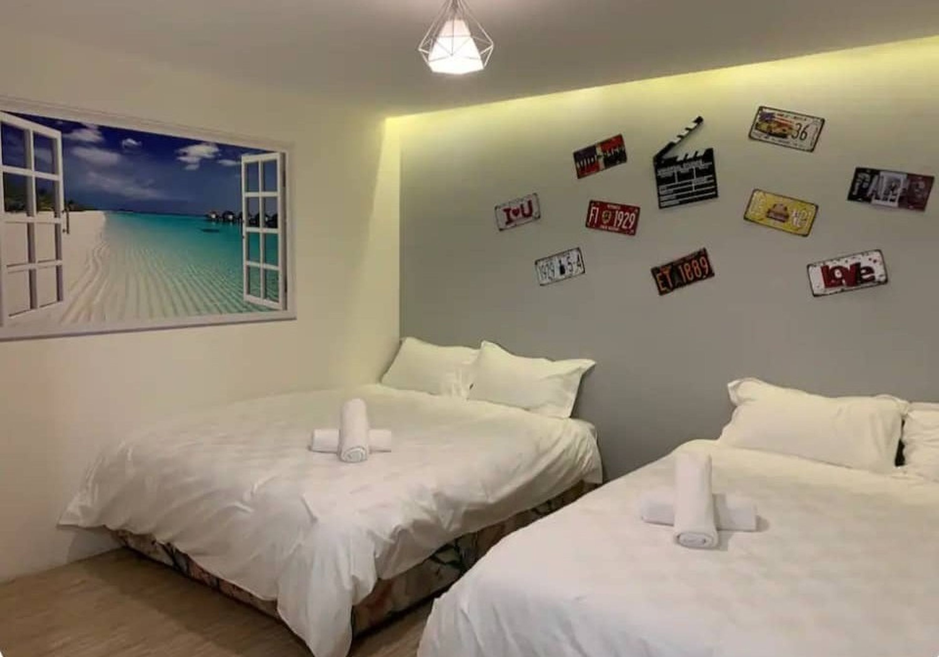 A hotel room with two beds, a view of the beach through an open window, and a wall decorated with vintage license plates.