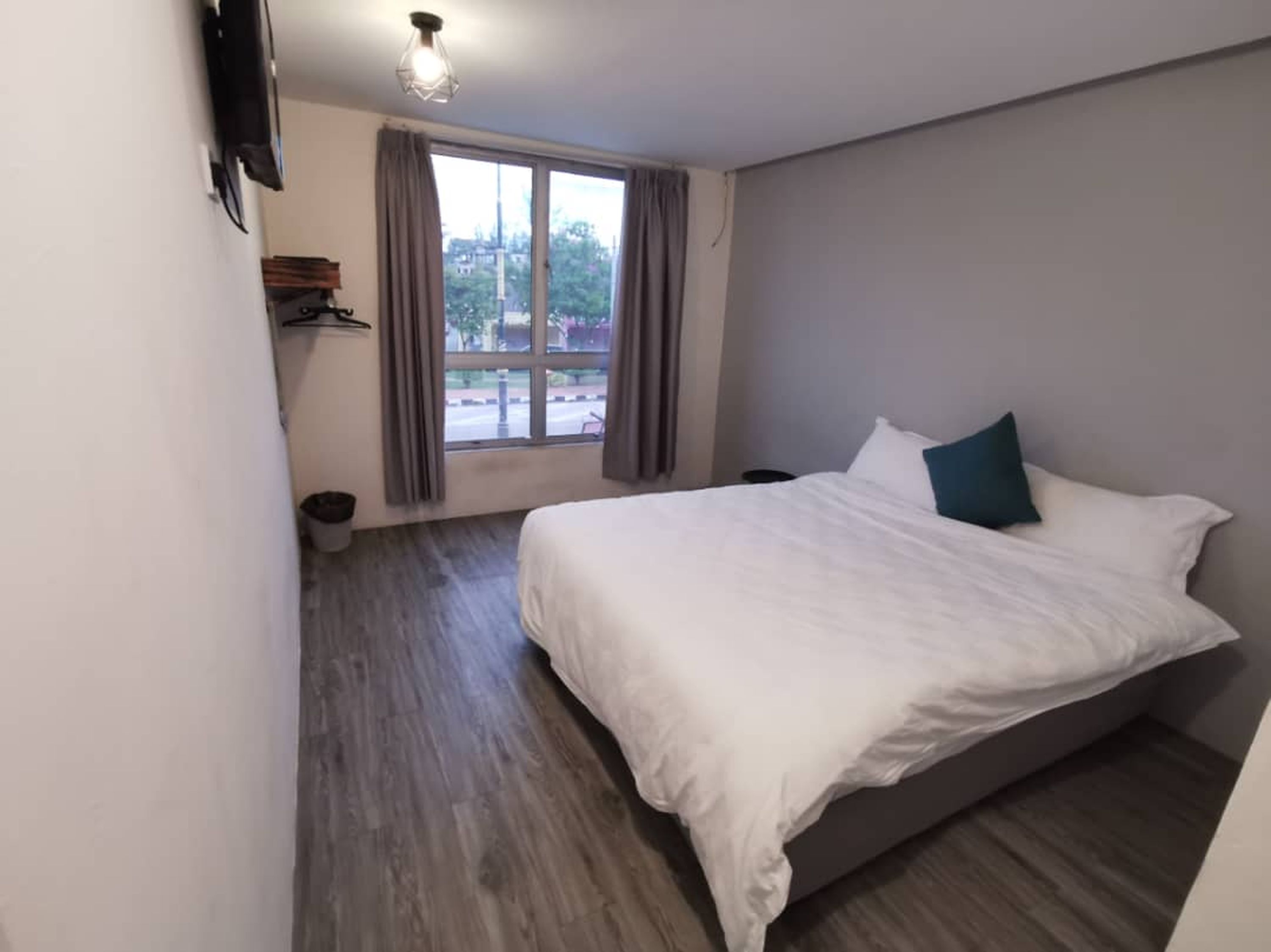 Un dormitorio con cama, ventana con cortinas, luz de techo y vista al exterior.