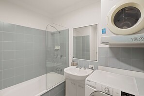 Un baño con bañera, lavamanos, ducha con mampara de vidrio y lavadora de carga frontal.