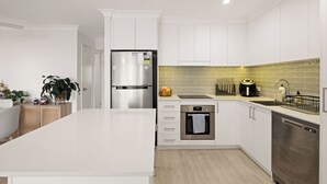 Eine moderne Küche mit weißen Schränken, einem Edelstahlkühlschrank, einem Backofen und einem Geschirrspüler.