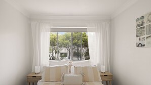 Ein Schlafzimmer mit großem Fenster, einem Bett mit gestreifter Bettwäsche, zwei Nachttischen mit Kerzen und einem Wandbild.