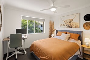 Un dormitorio con cama, escritorio, silla y ventilador de techo.