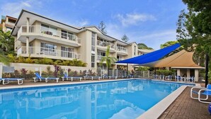 Ein Pool mit Liegestühlen, ein Gebäude mit Balkonen und ein blaues Sonnensegel.