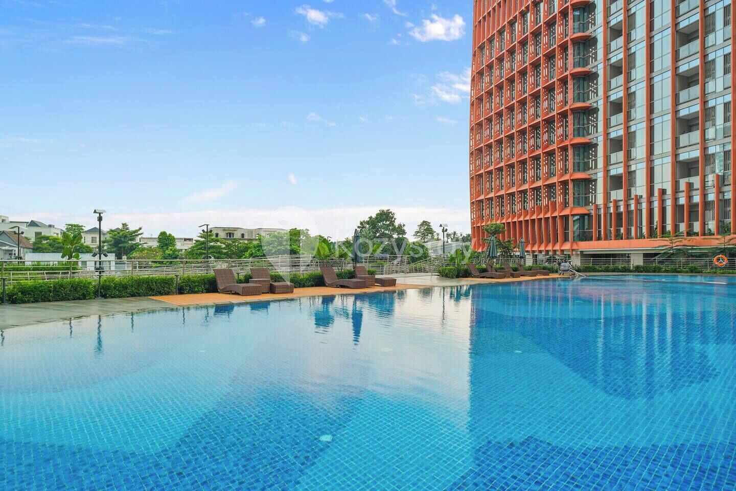 A swimming pool with lounge chairs, a tall red building, and a clear sky.