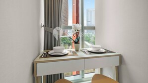 Habitación de hotel moderna con zona de comedor que presenta una mesa dispuesta con platos, cubiertos y un florero con flores.