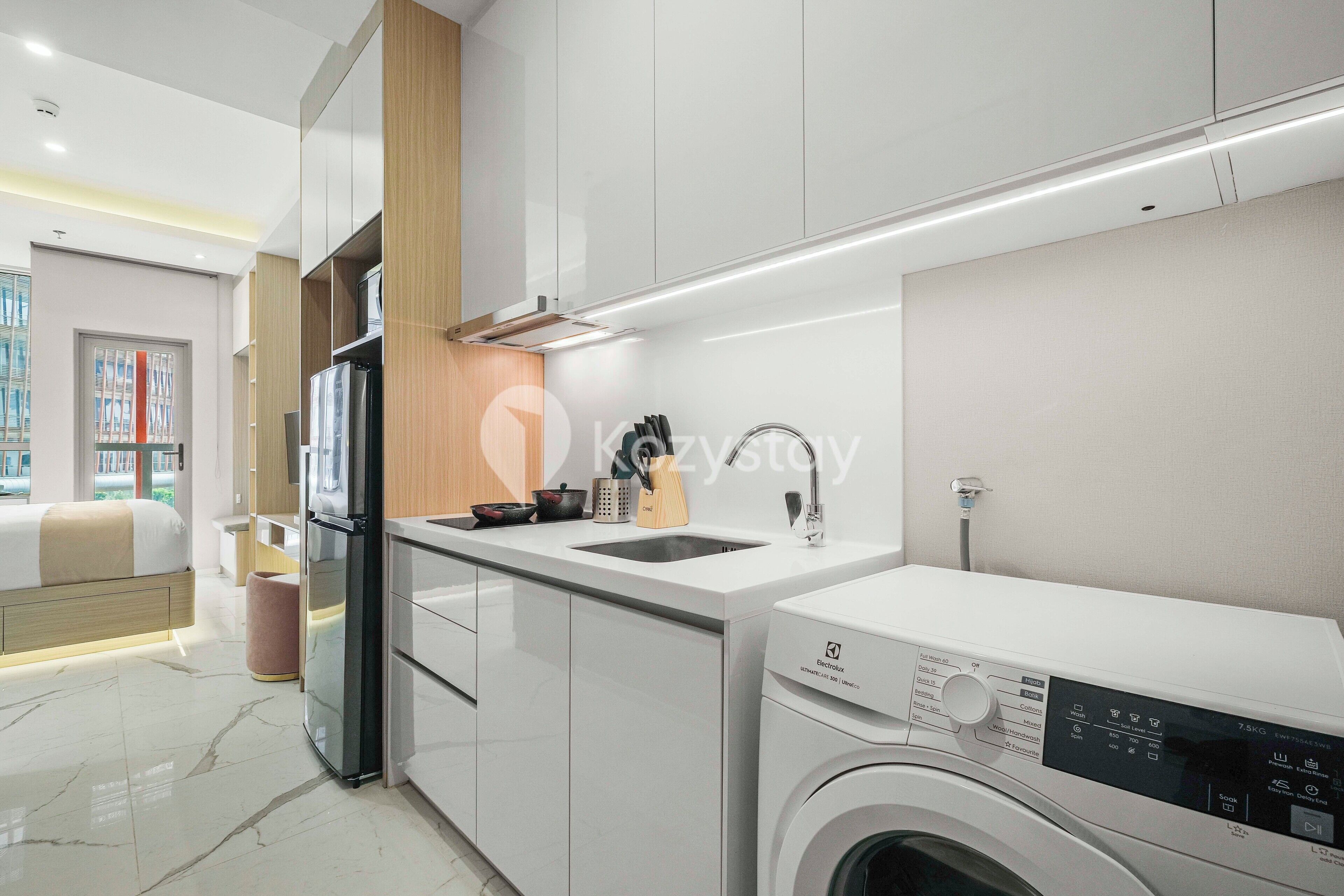 Una cocina moderna con lavadora integrada, un lavabo y una zona de comedor con cama.
