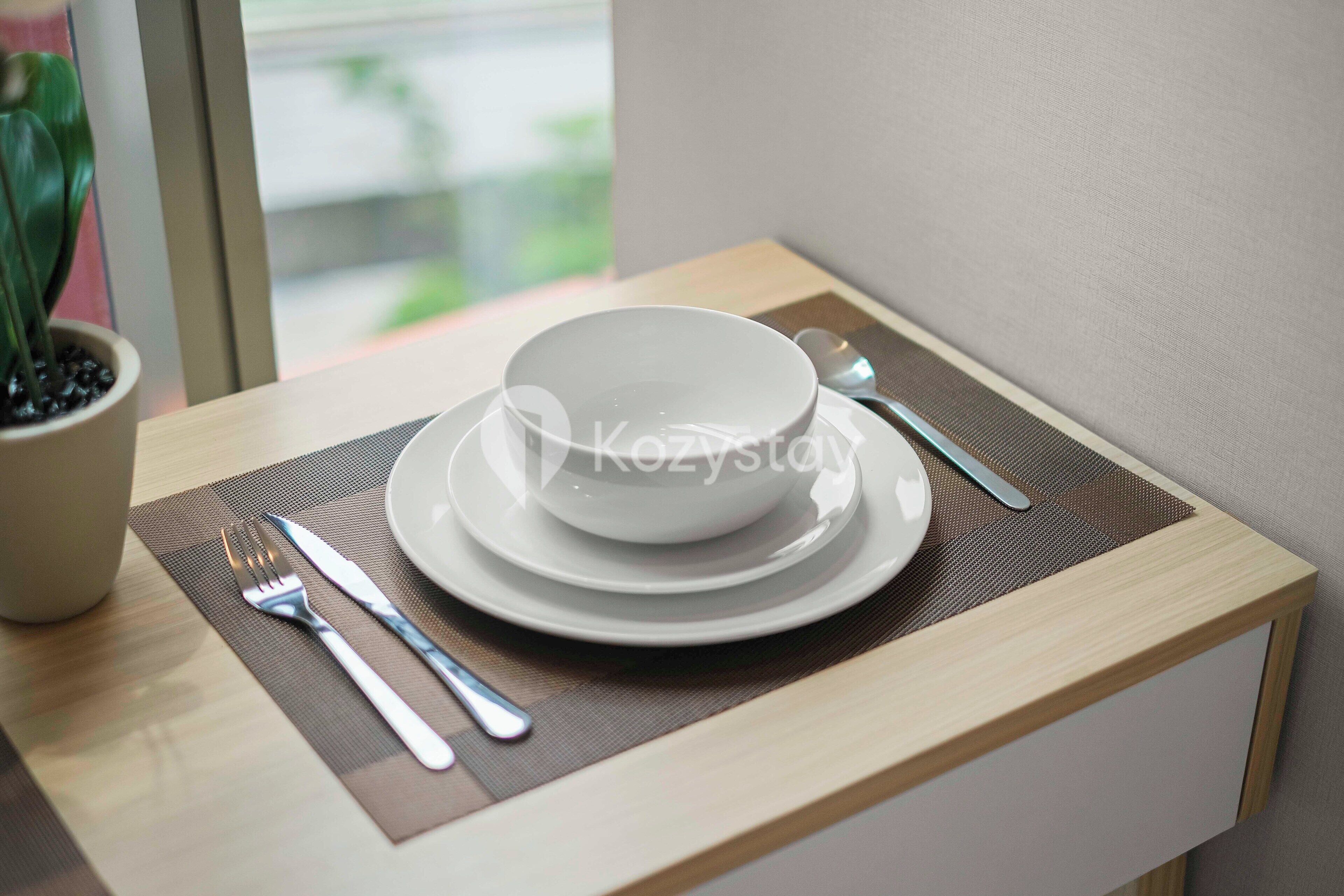 A neatly arranged dining setup with a bowl, plate, fork, and knife on a wooden table with a placemat.
