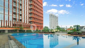 Una piscina con borde de baldosas, rodeada de edificios modernos con balcones y un cielo despejado.