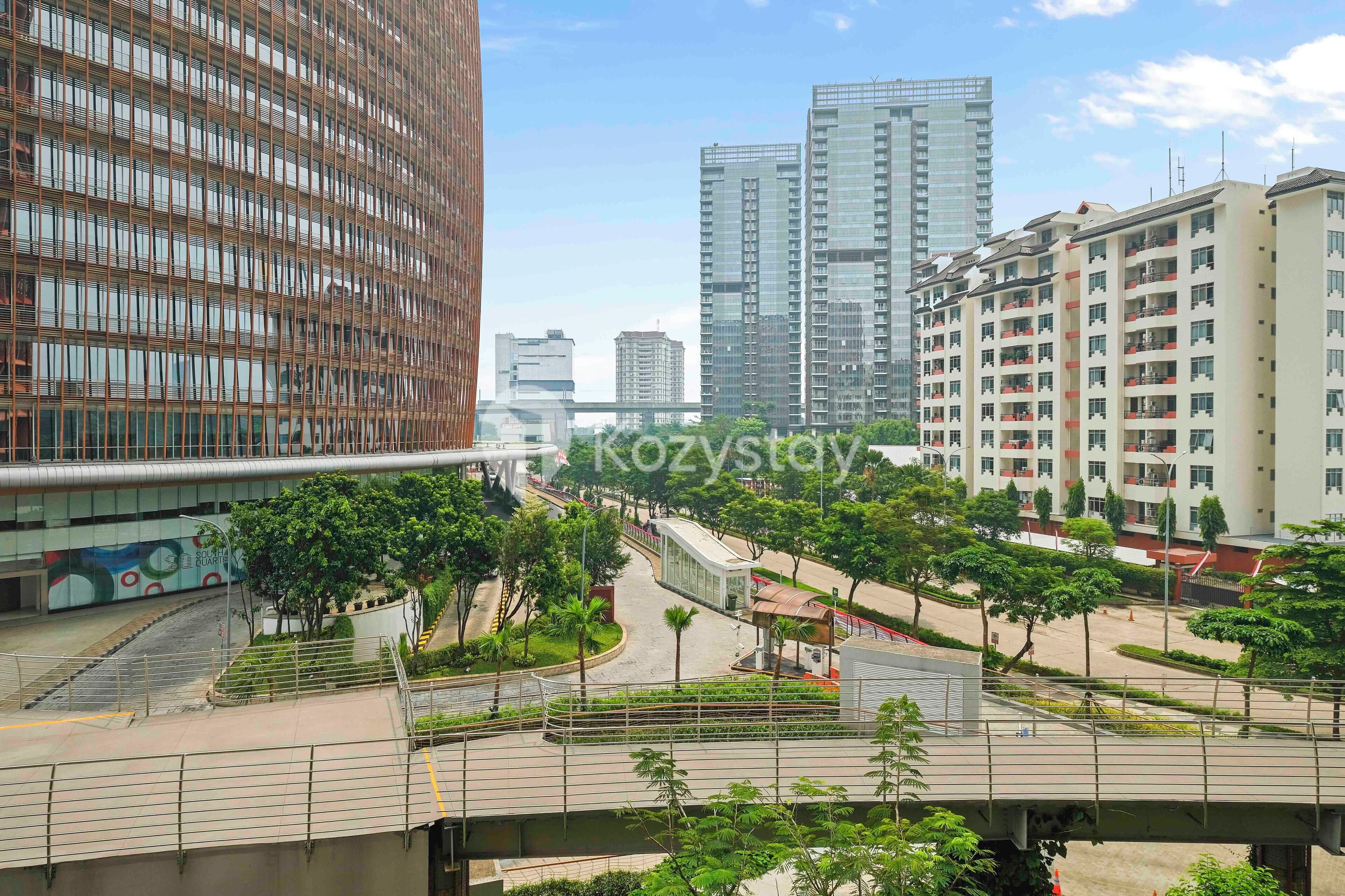 Una zona urbana moderna con edificios altos, un puente peatonal y áreas ajardinadas.