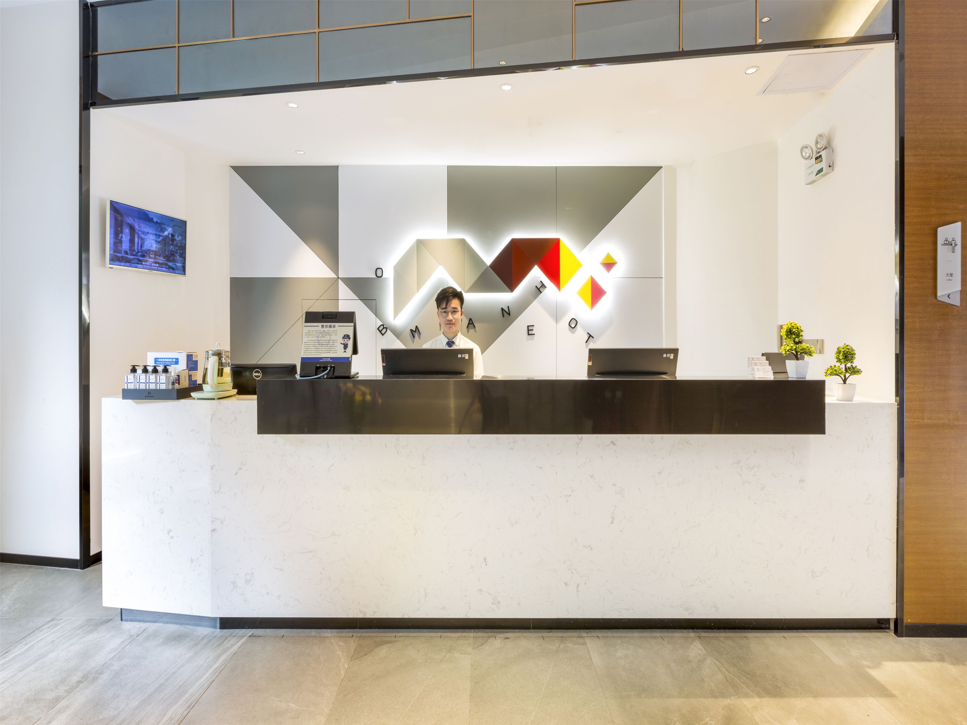A reception desk with a digital screen, a laptop, and a small plant.