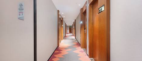 A hotel hallway with a patterned carpet, wooden doors, and a sign on the wall.