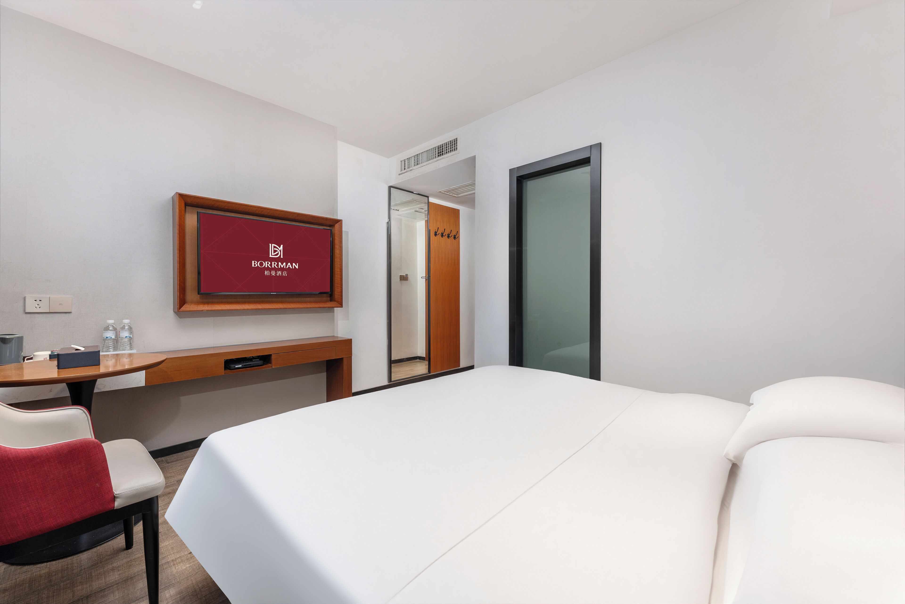 A hotel room with a bed, a desk, a chair, a mirror, and a television.