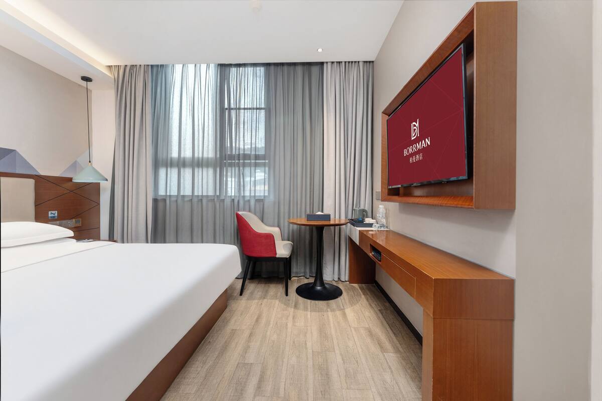 Habitación de hotel con cama, escritorio, silla, televisor y ventana con cortinas.