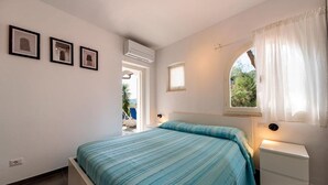 Una camera da letto con un letto, un comodino, una finestra con tende e quadri appesi al muro.