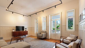 A spacious living room with a large flat-screen TV, a wooden cabinet, two armchairs, a sofa, and a grey rug. - Bonfim 241 Family House (Porto)