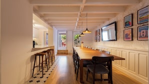 A long dining table with chairs, a kitchen area with stools, and a hallway leading to an outdoor area. - Bonfim 241 Family House (Porto)