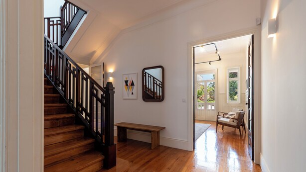 A wooden staircase with a black railing leading to an upper floor. A bench is placed at the bottom of the stairs. - Bonfim 241 Family House (Porto)