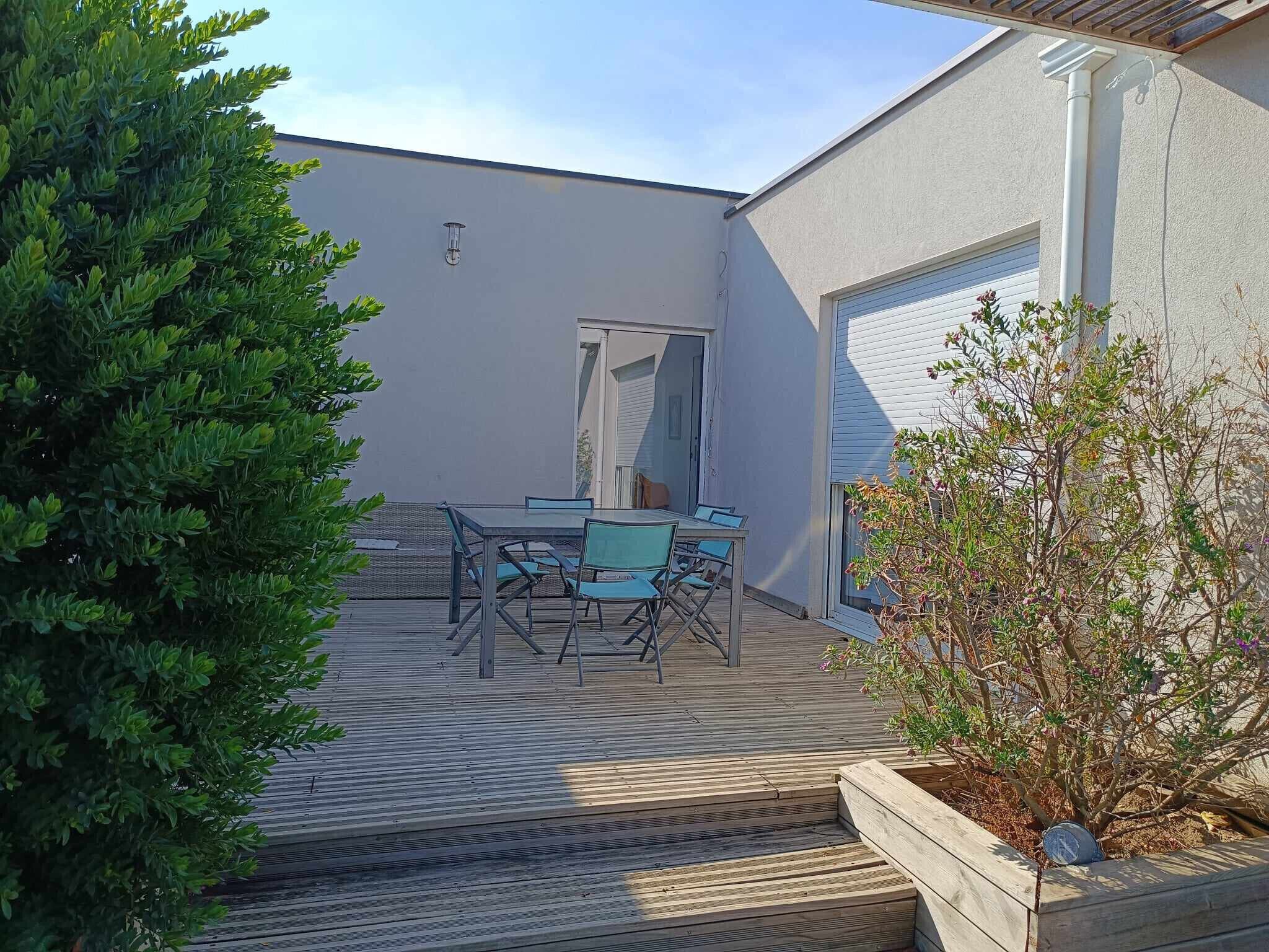 Une terrasse avec une table et des chaises, une plateforme en bois et une plante en pot.