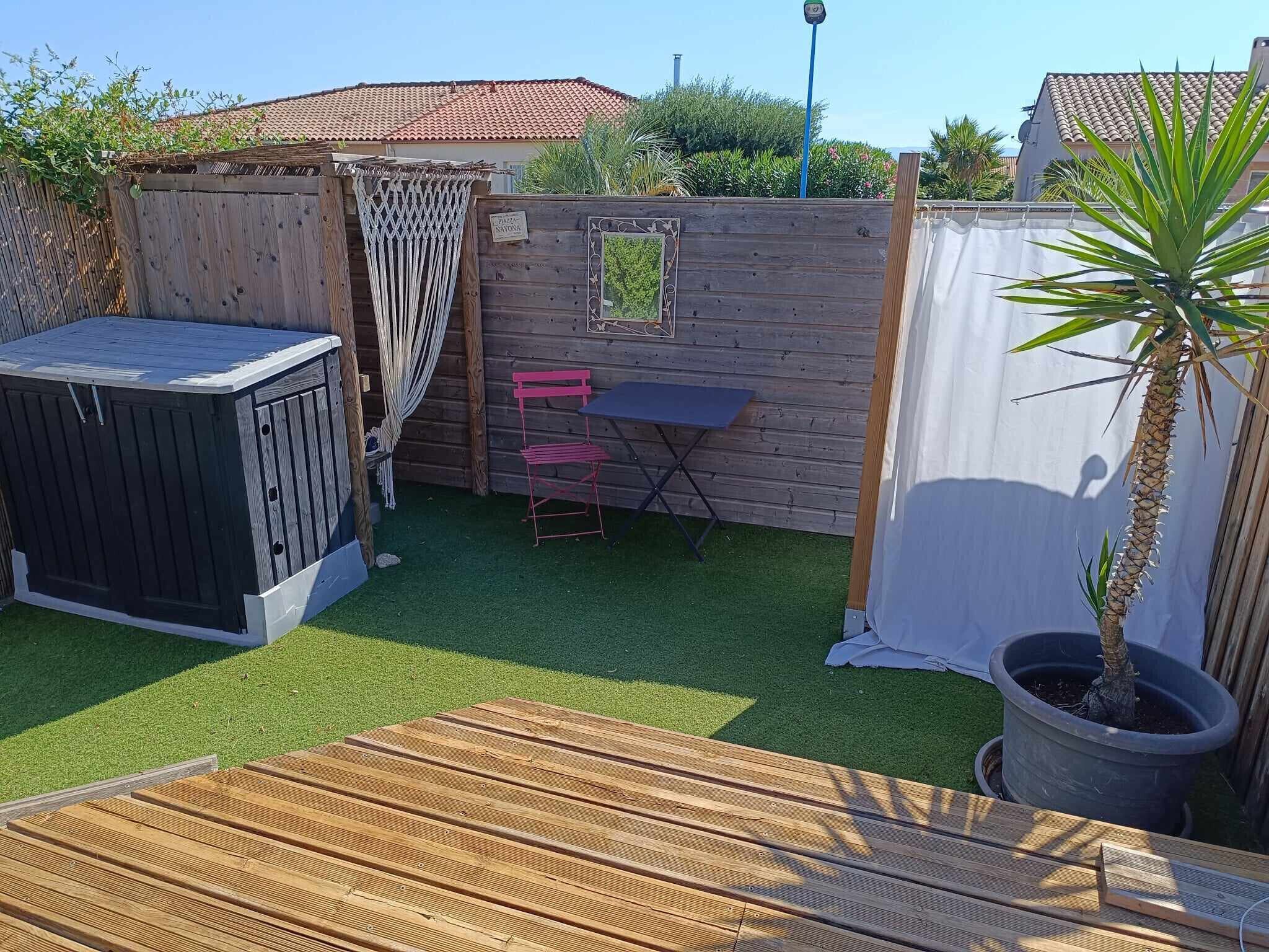 A wooden deck with a small table and chairs, surrounded by a wooden fence and a potted plant.