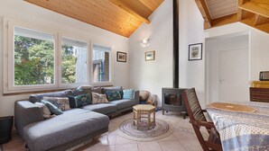 Una sala de estar acogedora con un sofá, una mesita, una silla, una chimenea y una ventana con vistas a árboles.