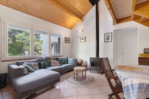 Una sala de estar acogedora con un sofá, una mesita, una silla, una chimenea y una ventana con vistas a árboles.