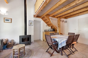 Ein gemütliches Wohnzimmer mit Kamin, Holzbalkendecke, einem Esstisch mit Stühlen und einer Treppe, die zu einer oberen Ebene führt.