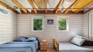 Una cabaña con dos camas, vigas de madera y ventanas que dan a vistas de vegetación.