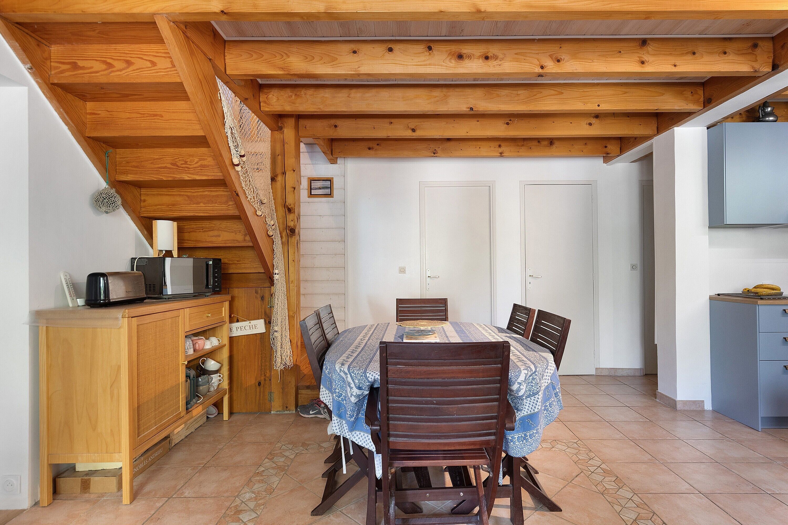 A dining area with a wooden ceiling, a table with chairs, a cabinet with kitchen appliances, and a door in the background.