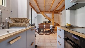 Una cocina moderna con vigas de madera, una zona de comedor con mesa y sillas, y un horno empotrado.