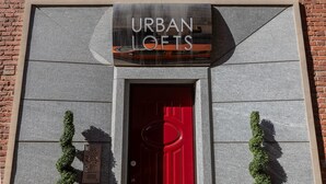Ein Gebäude mit einem Schild, auf dem "URBAN LOFTS" steht, über einer roten Tür, begleitet von zwei grünen Pflanzen.