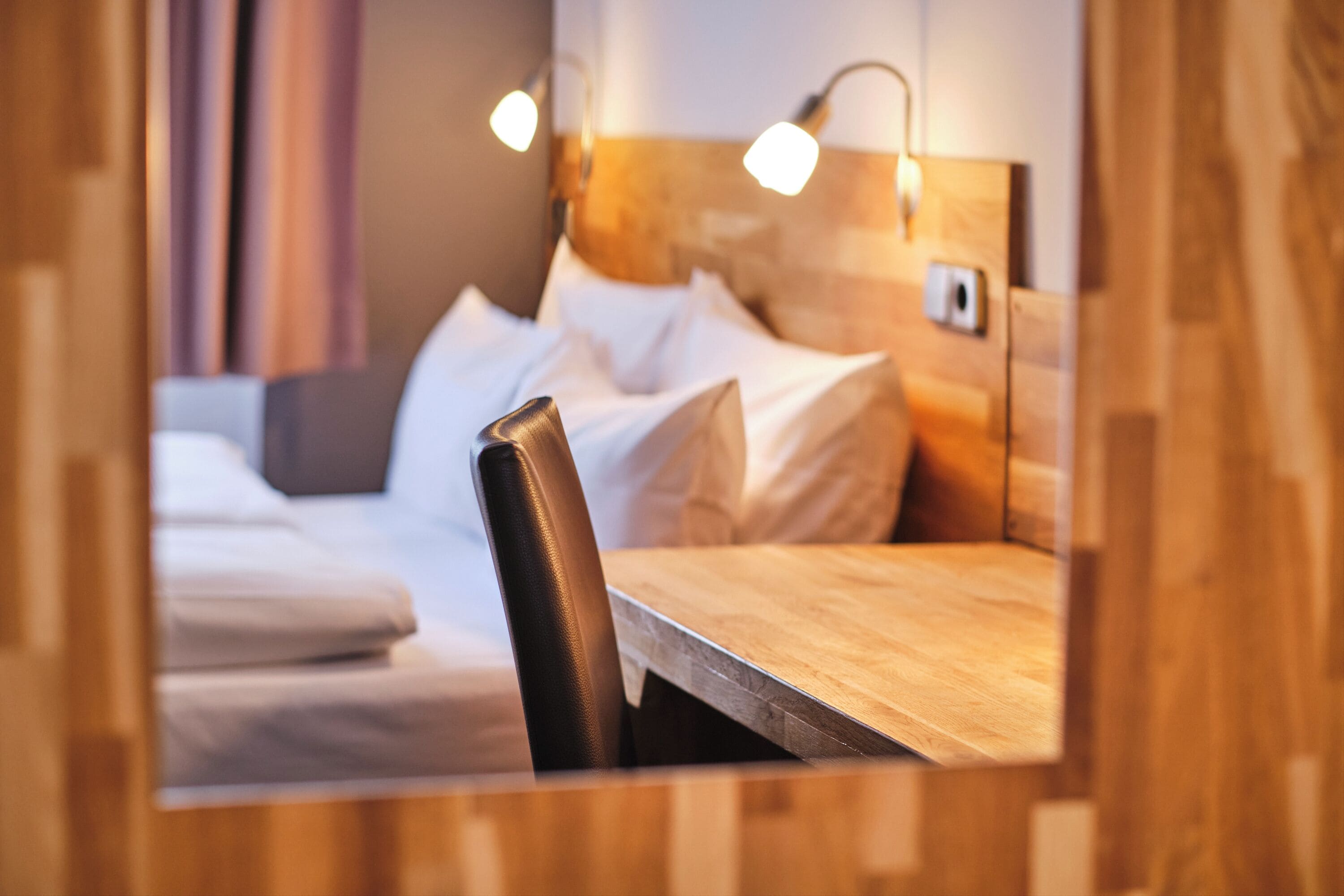 A hotel room with a wooden headboard, a wooden table, and a bed with white linens.