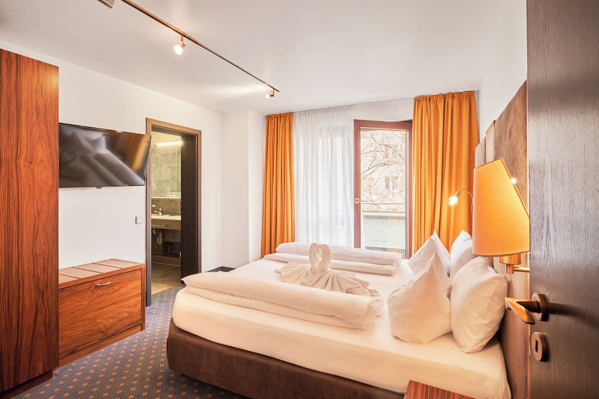 A hotel room with a bed, a wooden wardrobe, a bathroom, and a window with curtains.