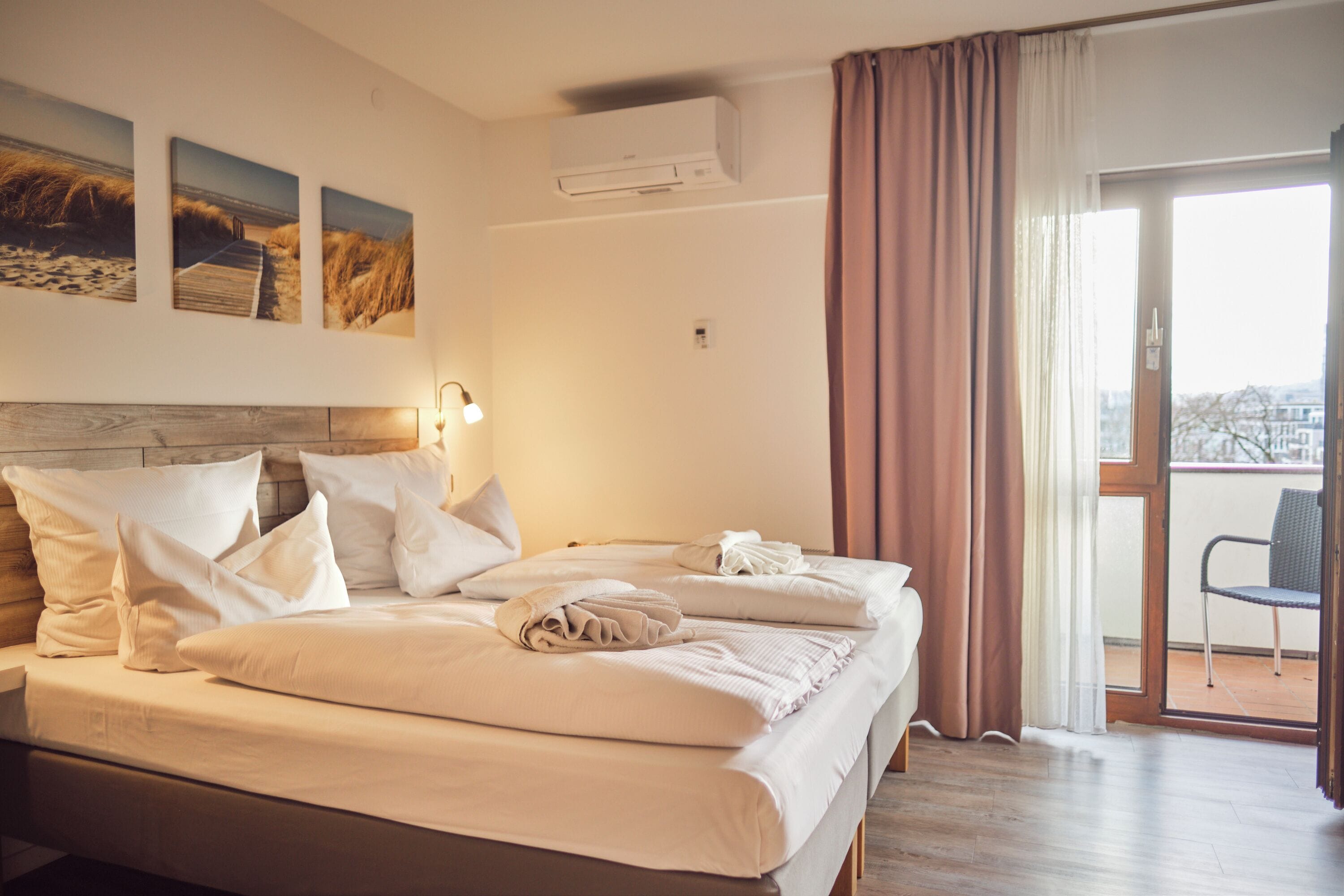 Habitación de hotel con dos camas, cabecero de madera, una ventana grande con cortinas y vistas a la ciudad.