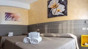 A hotel room with a large bed, two pillows, and a folded towel on the bed. There is a painting on the wall and a yellow cabinet in the corner.