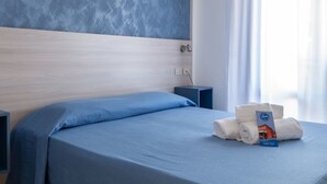 A hotel room with a bed, a painting, an air conditioner, a nightstand, and a window with curtains.