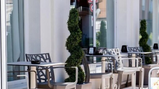 An outdoor seating area with tables and chairs, a potted plant, and a glass railing.