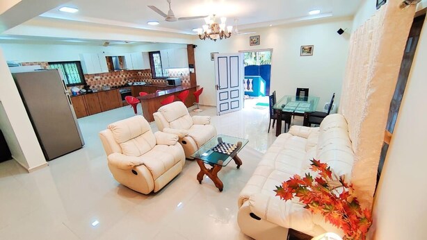 A spacious living room with a sofa set, a glass coffee table, and a dining area in the background. - Spring Field Villa (Orlim)