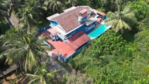 A large house with a red roof, surrounded by lush greenery and palm trees. - Spring Field Villa (Orlim)
