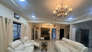 A spacious living room with two white sofas, a glass coffee table, a TV mounted on the wall, and a chandelier. - Spring Field Villa (Orlim)