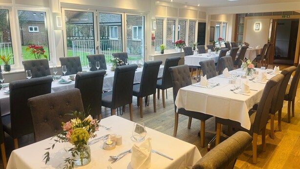 A restaurant with multiple tables set for dining, large windows, and a view of the outside.