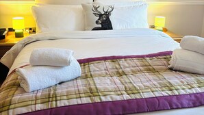 A neatly made bed with a plaid bedspread and two pillows, one with a deer print. There is a painting of a forest on the wall above the bed.