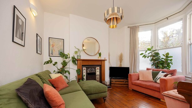 Uma sala de estar com um sofá verde, uma poltrona rosa, uma lareira e uma televisão.
