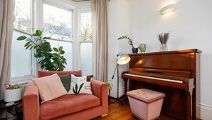 Um quarto aconchegante com piso de madeira, um sofá rosa, um piano e um vaso de planta.