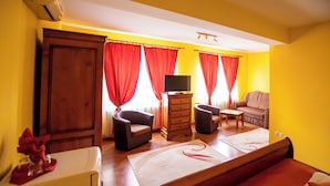A hotel room with a bed, two armchairs, a sofa, a TV on a wooden stand, and red curtains. - Noroc si Fericire (Târgu Mureș)