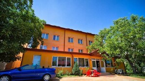 A two-story building with a yellow facade, a blue car parked in front, and a red table and chairs in the courtyard. - Noroc si Fericire (Târgu Mureș)