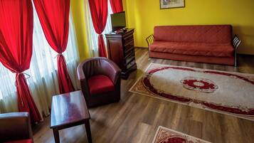 Een kamer met een houten vloer, rode gordijnen, een rode bank, een fauteuil, een houten tafel en een televisie op een houten kast.