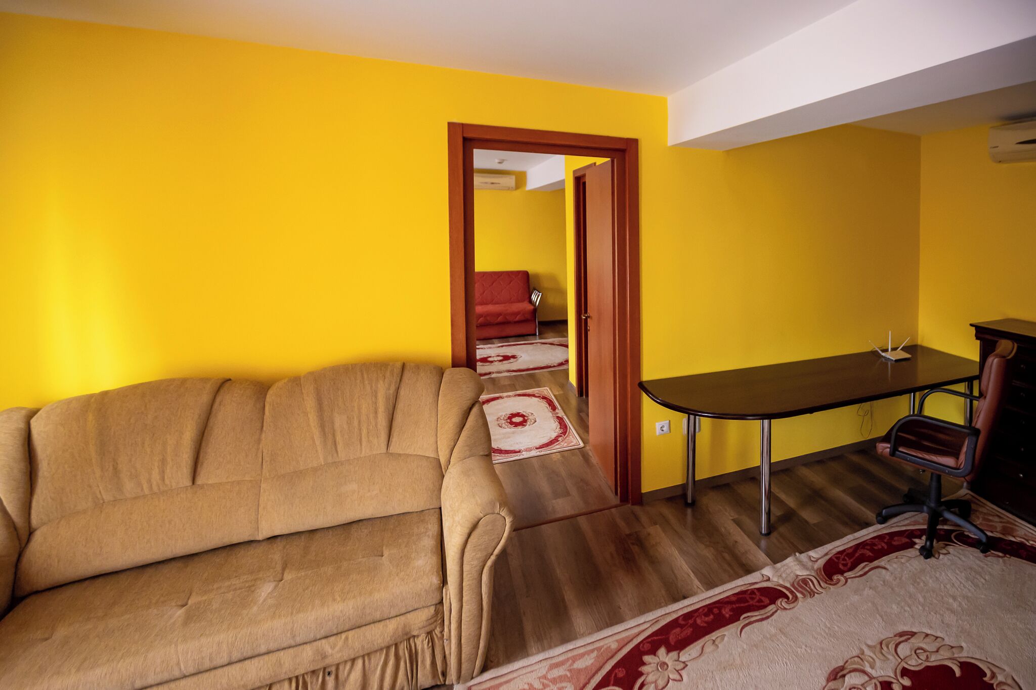 Una habitación con paredes amarillas, un sofá marrón, una mesa de madera y una silla roja.