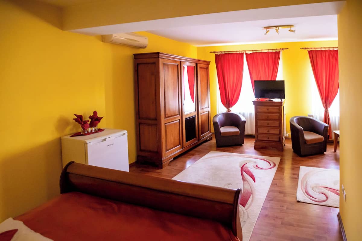 A room with a bed, a wooden wardrobe, a television on a stand, and a desk with a chair.